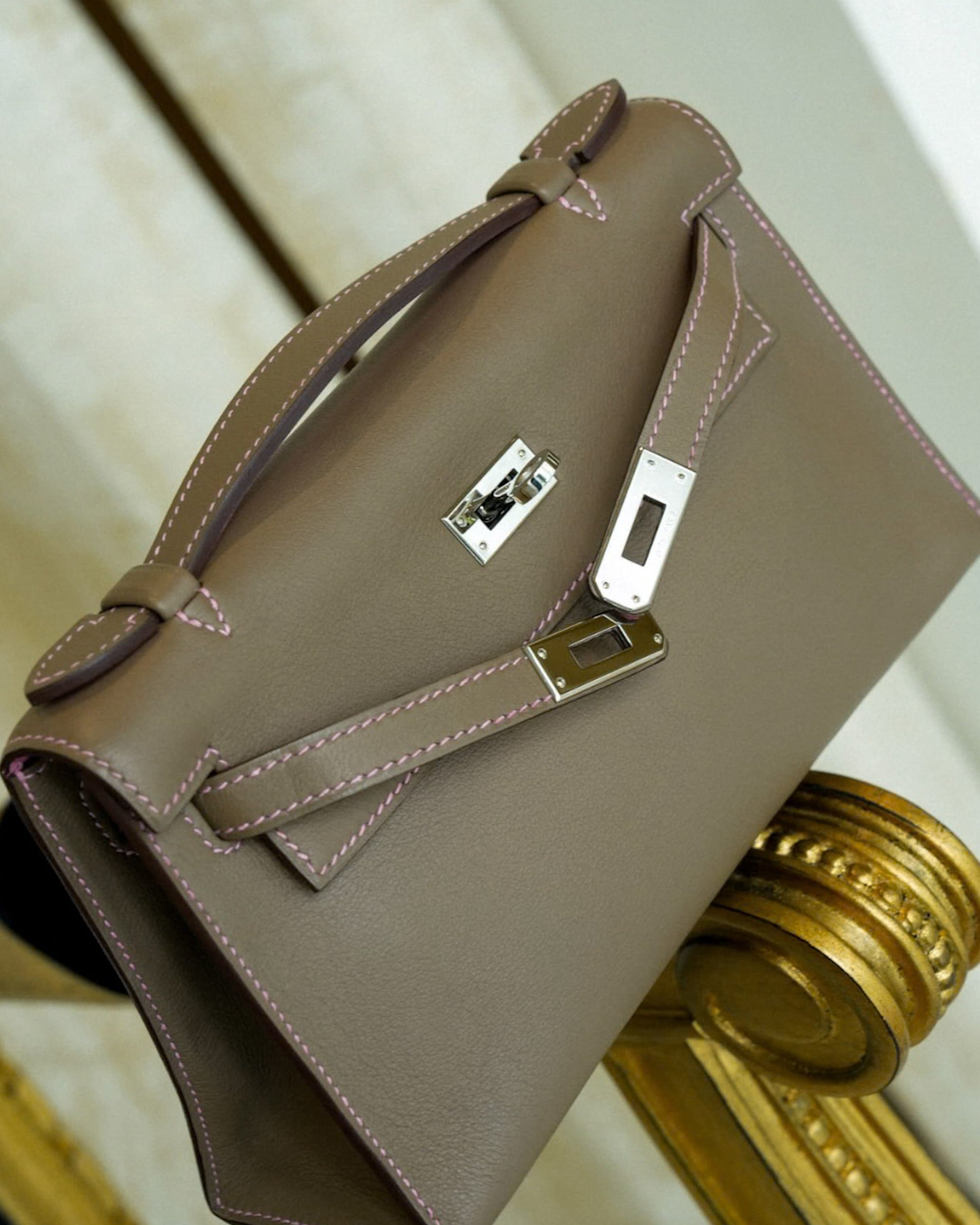 Hermès Kelly handbag, black leather, gold hardware, held by a client. Editorial imagery, availability varies.